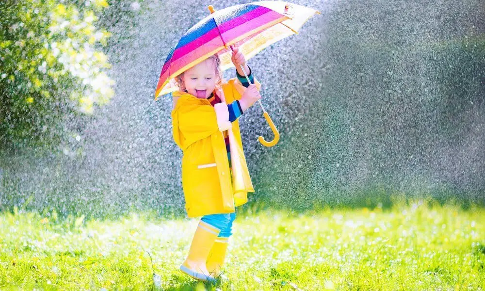 Funny toddler with umbrella playing in the rain, pink and purple